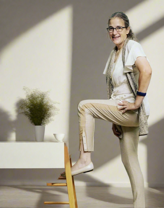 Elderly woman wearing adaptive pants and placing her leg on a stool while smiling for the cameras.