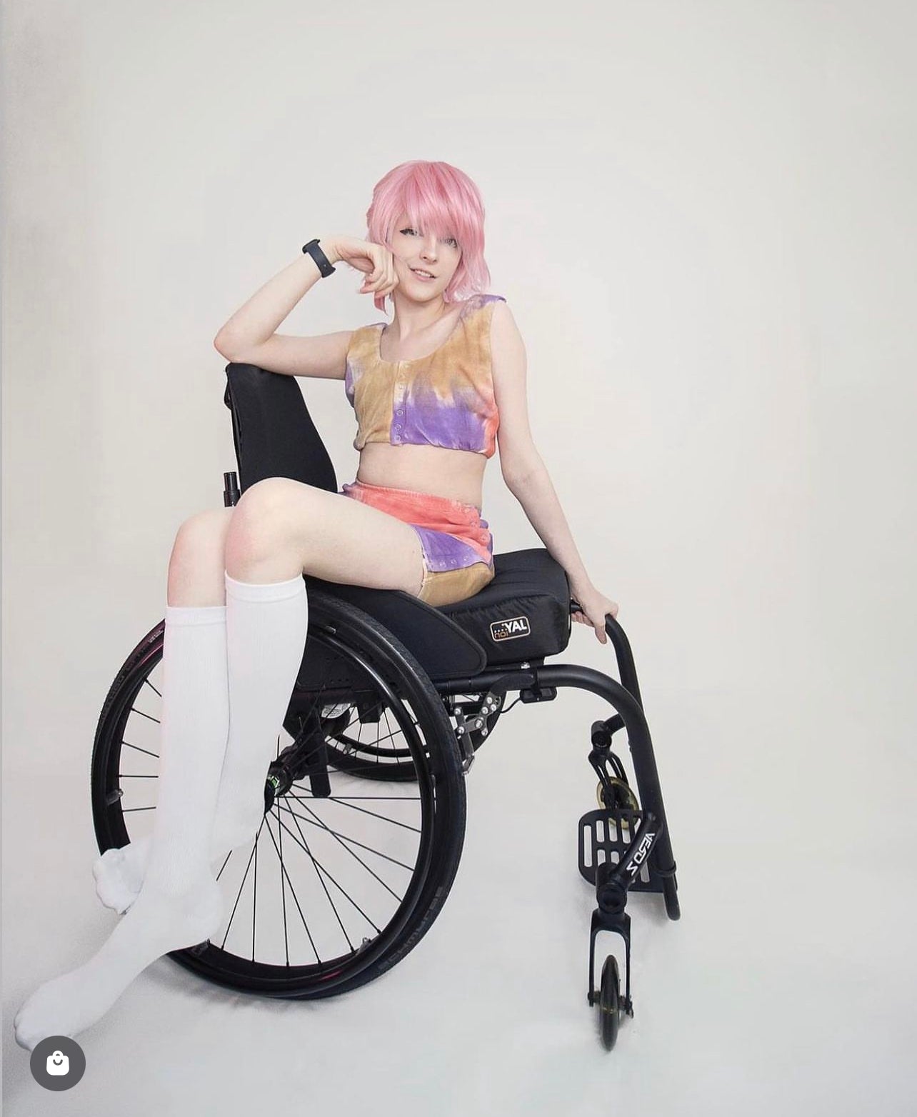 Woman sitting on wheelchair with her legs to the side of it, wearing colorful adaptive clothing